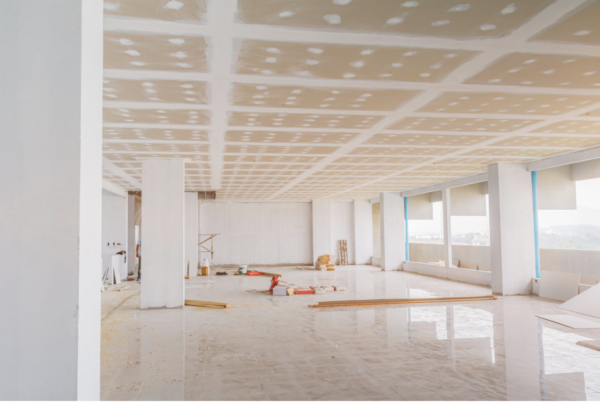 Picture is of an entire floor of an office building that is under construction. There are ladders, half-finished drywall, and painters tape all over the walls still. It looks more like a construction scene than just solely a painting project. 